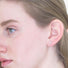 Model wears a tiny silver  X  stud earring in her earlobe