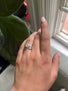 A woman is wearing an oval diamond ring and a complementary wedding band decorated with hand engraved flowing lines.