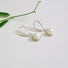 A round 6 mm white genuine pearl is set into an organic shaped rim of silver  which is suspended from a silver ear hook.