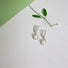 A round 6 mm white genuine pearl is set into an organic shaped rim of silver which is suspended from a silver ear hook.