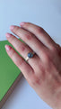 A woman is wearing a ring with the band made to look like it is wrapped around the finger, The band is a -symmetrical and hand textured with small horizontal lines .  On top of the ring is an 8mm blue green flashy labradorite cabochon stone.