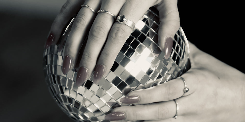 woman hands hold a small silver disco ball. Her fingers show handmade silver rings with gemstones. 