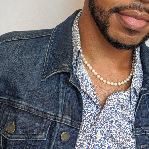 Closeup of a man's neck showing a relaxed and sophisticated strand of consciously sourced white freshwater round pearls.