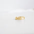 A textured band in 14 karat yellow gold lies on a white surface. .The band is made to look like birchbark. 
