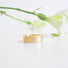 A textured band in 14 karat yellow gold lies on a white surface. .The band is made to look like birchbark. 