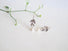 A sprig of leaves dangle down to a white round pearl which  is at the end of the sprig leaf