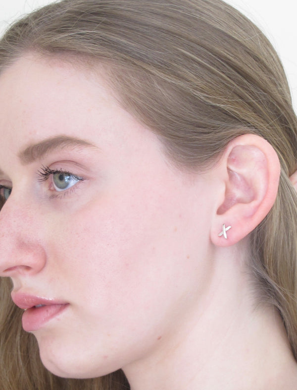 Model wears a tiny silver  X  stud earring in her earlobe