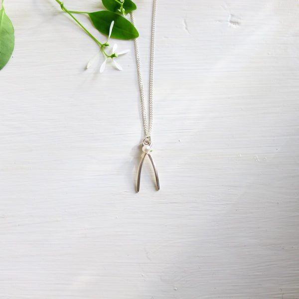 A delicate wishbone shaped sterling silver pendant accented with a small  3 mm white freshwater pearl at the crossover of the wishbone . 