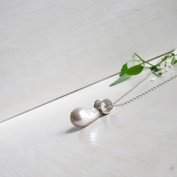 A large irregular non  spherical  genuine freshwater Baroque pearl hangs  from a unique textured silver flared tube that  a long silver chain threads through.  