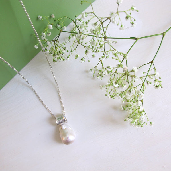 A large irregular non  spherical  genuine freshwater Baroque pearl hangs  from a unique textured silver flared tube that  a long silver chain threads through.  