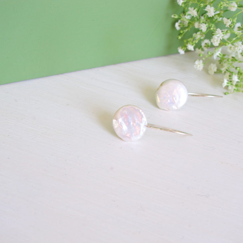 A pair of white genuine freshwater round  10 mm wide coin pearls with a silver ear hook. 