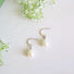 A pair of silver earrings with a white freshwater genuine oval pearl dropping from a curved crescent with an ear post.