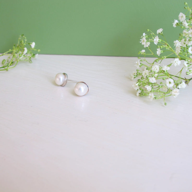 Genuine round  6 mm white pearls are nestled into a  round silver rimmed setting with a post.