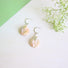 A large genuine teardrop shaped freshwater pink y hued coin pearl dangles from a handcrafted silver crescent stud earring