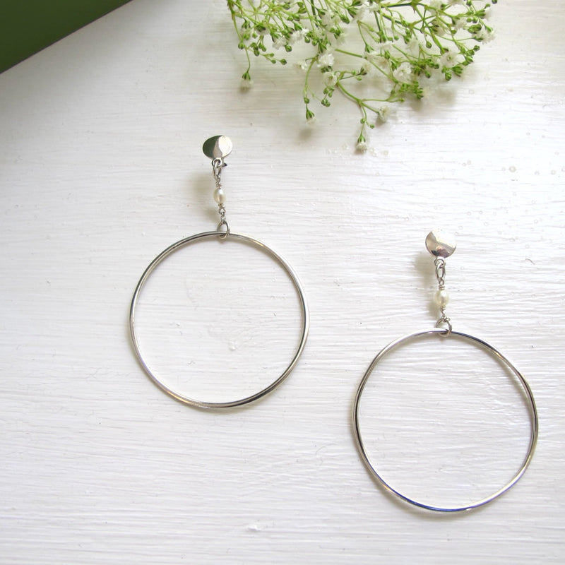 From small silver discs with ear posts drops a short chain with a pearl  that connects a handcrafted large silver hoops.