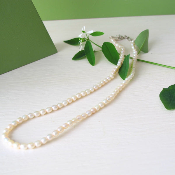 A  hand strung genuine pearl necklace  composed of small  
 white luminous oval freshwater pearls.