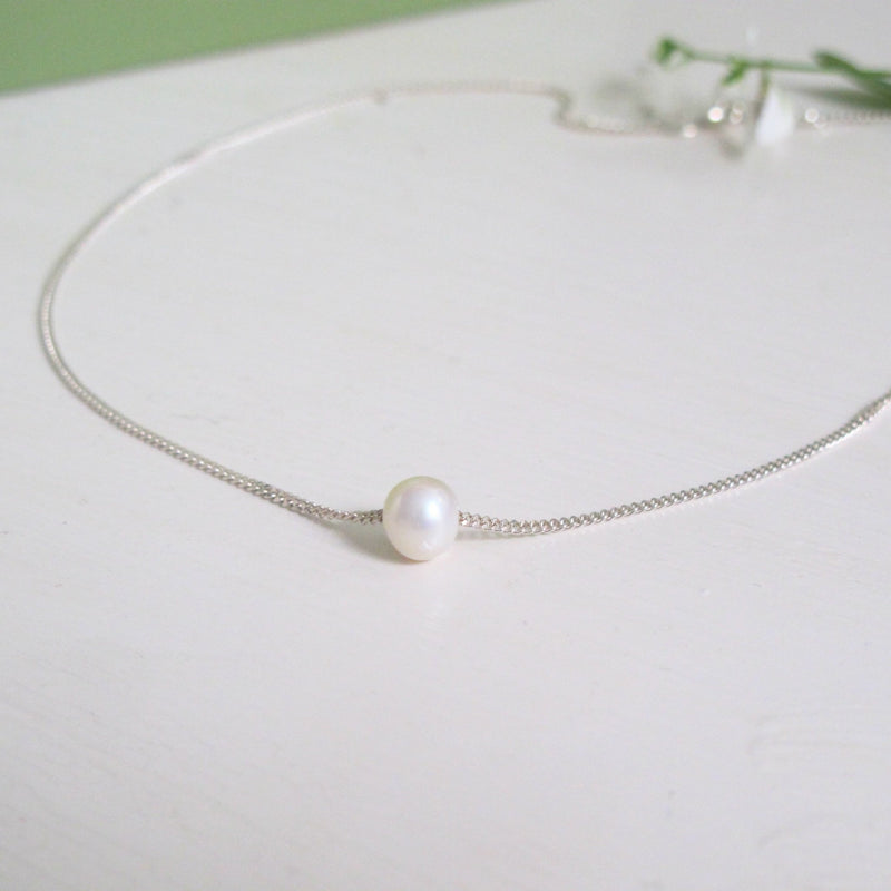 A genuine round white freshwater pearl is threaded onto a Reiki imbued silver curb chain.