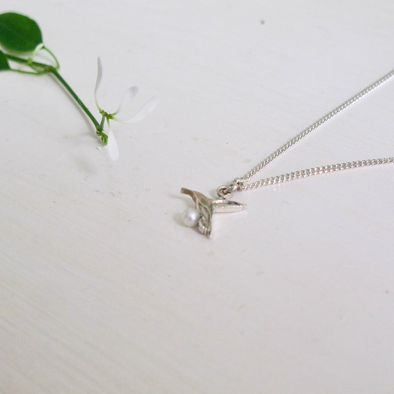 A 10 mm Hummingbird depicted in flight hangs from a silver chain.  A tiny pearl sits at the bottom of the bird's breast.