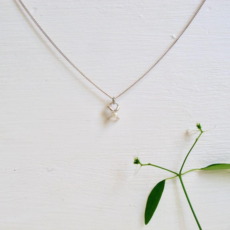 A sterling silver chain has a delicate and small  X shape charm hanging from it. The X is designed to symbolize a Kiss! The kiss is sealed with a 3 mm round genuine pearl that sits in the middle of the X.  The pendant measures approximately 10 mm x 8 mm