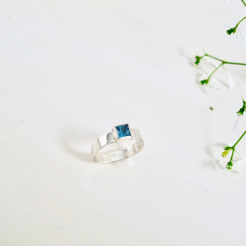 Facing you is a sterling silver ring with 5x5 mm gorgeous London Blue Topaz  which is set into a sterling silver square bezel. The square theme is echoed with the 4 mm wide square band.  The ring has a very modern appearance. 