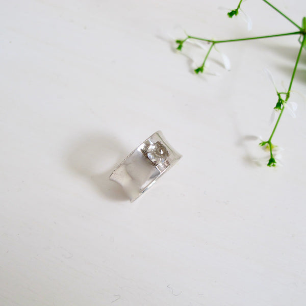 This ring is called Big Beauty and lives up to its name with a 10 mm wide, slightly concave band. Nestled in the middle of the band is a prong set 6 mm rose-cut white topaz stone.  It is a very modern and elegant looking ring 