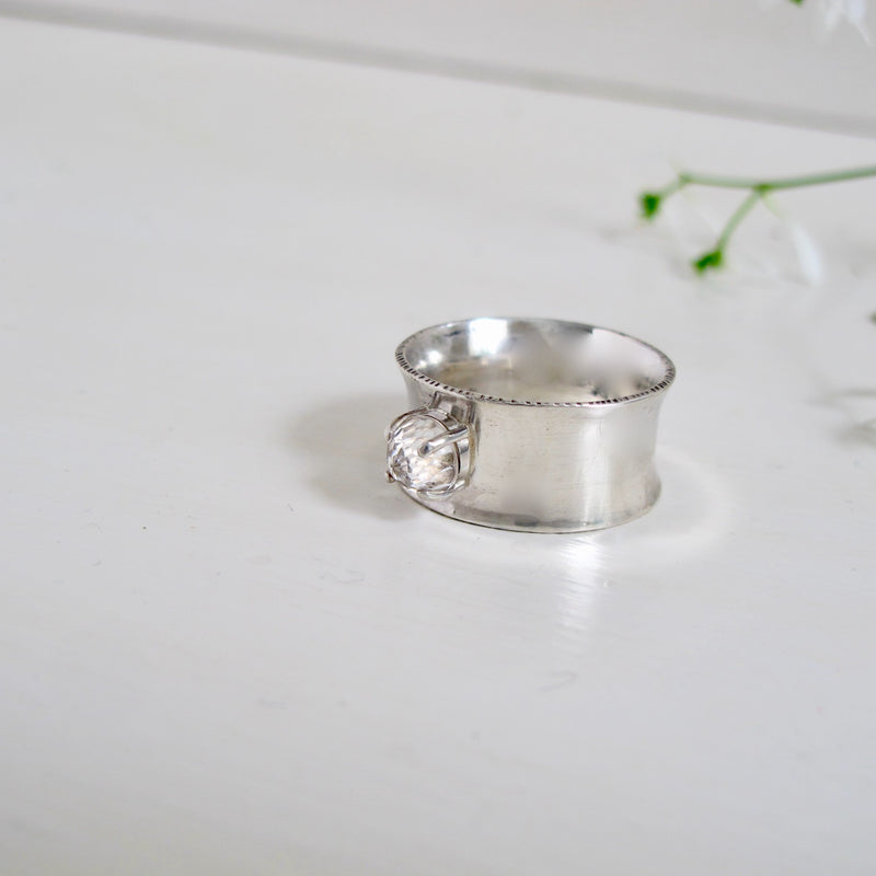 This ring is called Big Beauty and lives up to its name with a 10 mm wide, slightly concave band. Nestled in the middle of the band is a prong set 6 mm rose-cut white topaz stone.  It is a very modern and elegant looking ring 