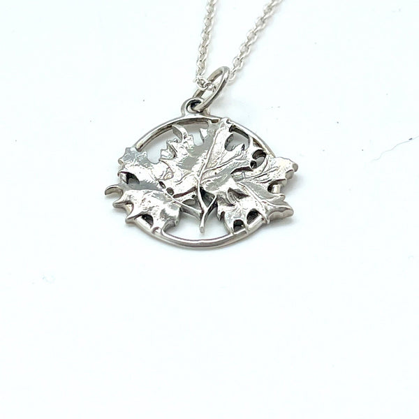 A  sterling silver pendant composed of three intertwined maple leaves which are contained by an open circle of silver. 
