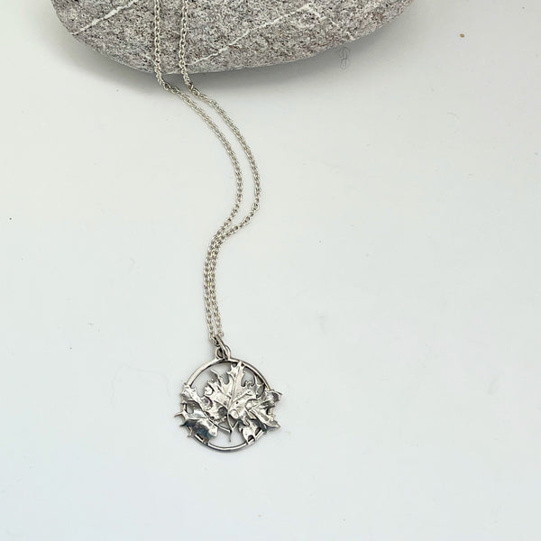 A  sterling silver pendant composed of three intertwined maple leaves which are contained by an open circle of silver. 
