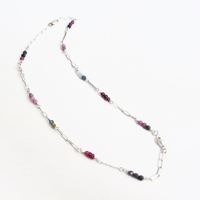 Authentic gemstones: Blue topaz, Garnets, Rhodolite garnets. Rubies  Sapphires and genuine pearls are arranged in an artful and asymmetrical design on a sterling silver paper clip link chain