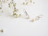 A sprig of leaves dangle down to a white round pearl which  is at the end of the sprig leaf.