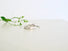 Two silver rings lie on a white surface. One ring with oval diamond on a slender band. One is textured to look like birchbark