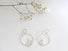 A medium size hoop earring in silver that is accented by a sprig of laurel leaf at the base of the hoop and a white pearl