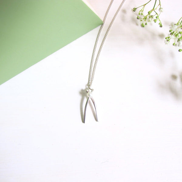 A delicate wishbone shaped sterling silver pendant accented with a small  3 mm white freshwater pearl at the crossover of the wishbone . 