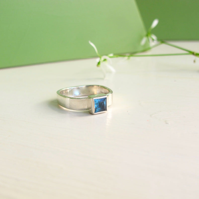 Facing you is a sterling silver ring with 5x5 mm gorgeous London Blue Topaz  which is set into a sterling silver square bezel. The square theme is echoed with the 4 mm wide square band.  The ring has a very modern appearance. 