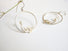 A pair of hoop earrings with sprig of laurel leaves dangling and a white round pearl which is at the end of the sprig leaf.
