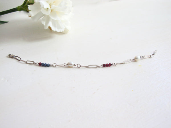 A paper clip link bracelet made up of Blue Sapphire, Genuine Pearl, and Deep Red Garnet beads.  Measures 7.50 "  Can be adjusted to size. 