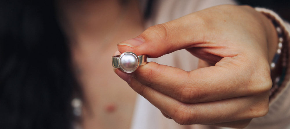 A large round white pearl set into a bezel with a wide silver band.