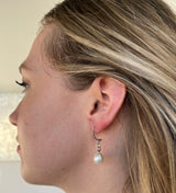 A pair of silver earrings with a white oval pearl dropping from a curved crescent with an ear post at one end of the crescent