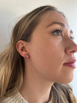 The earlobe of a model shows her wearing a reiki imbued X  with a small consciously sourced pearl in the middle of the X