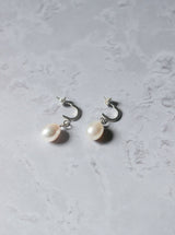 A pair of silver earrings with a white oval pearl dropping from a curved crescent with an ear post at the end of the crescent