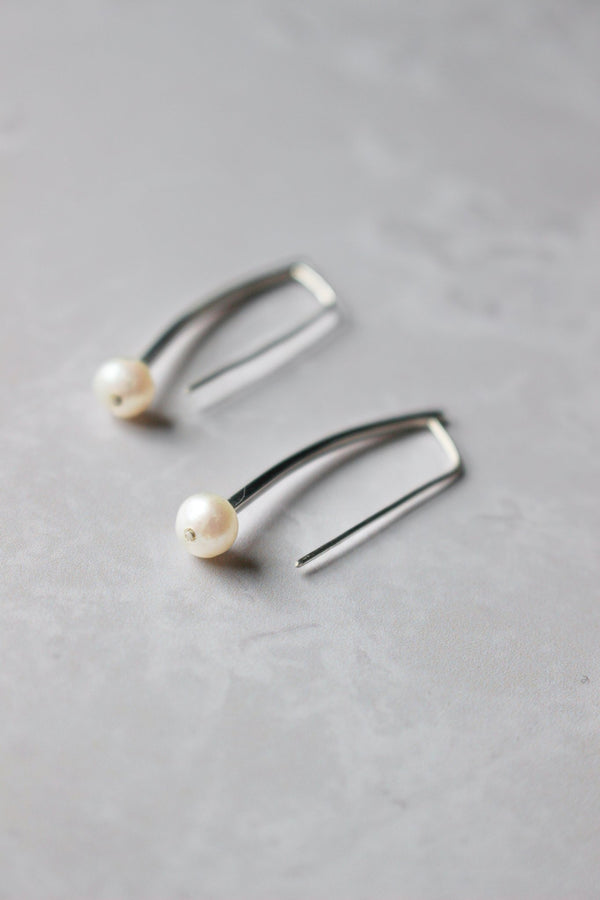 A slightly curved 1 " long silver bar hangs from the earlobe. At the bottom of the bar is a small white round pearl.