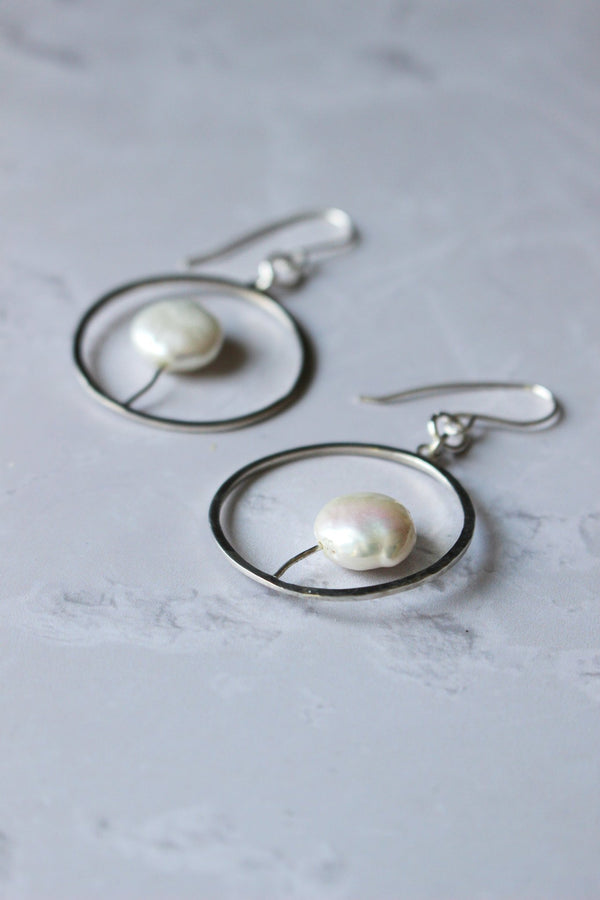 A hoop earring. In the centre of the circle hoop, on top of the slightly bent wire, is a 10mm coin pearl. Imbued with Reiki.