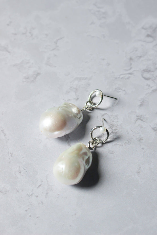 A large Baroque pearl dangles below a soft-edged silver halo stud with a tiny pearl adorning the top.