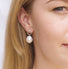 A woman’s earlobe shows a Baroque pearl dangling from a soft-edged silver halo with a tiny pearl adorning the top.