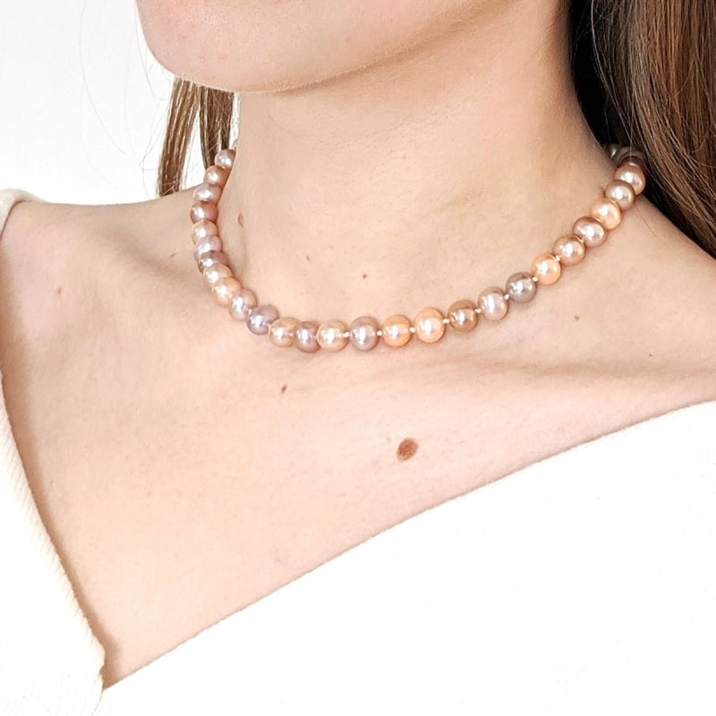 A woman’s wears an elegant neck-hugging strand of Reiki imbued round pearls naturally ranging from off-white to pinks.