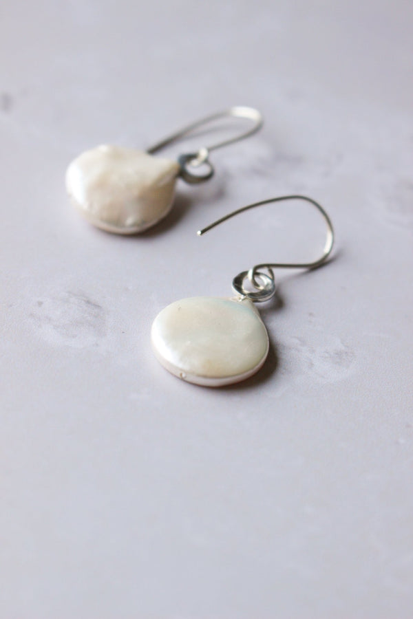 White coin pearl earrings, reiki imbued  have an irregular round shaped silver ring through which the ear hook is attached.