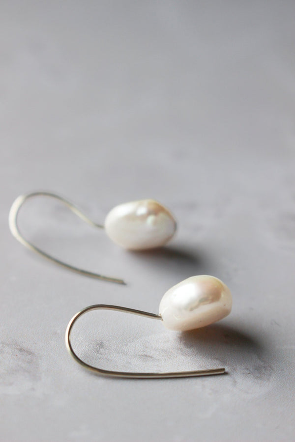 a pair of white round coin pearls with a fixed silver ear hook. 