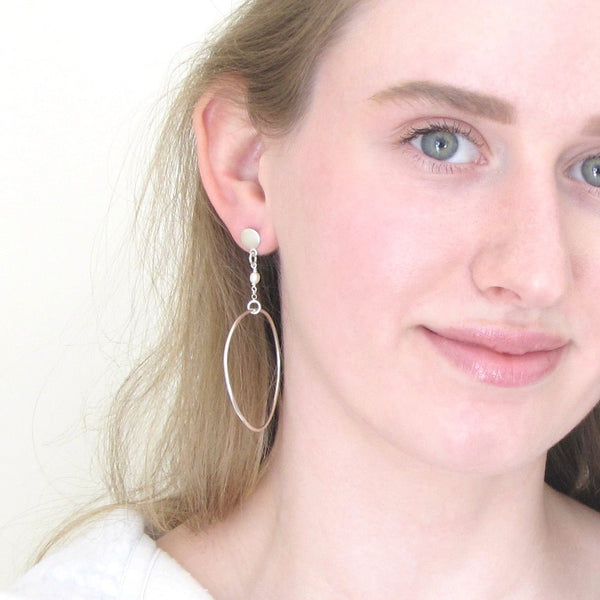 model wears handcrafted silver hoops that fall between the earlobe and the clavicle.