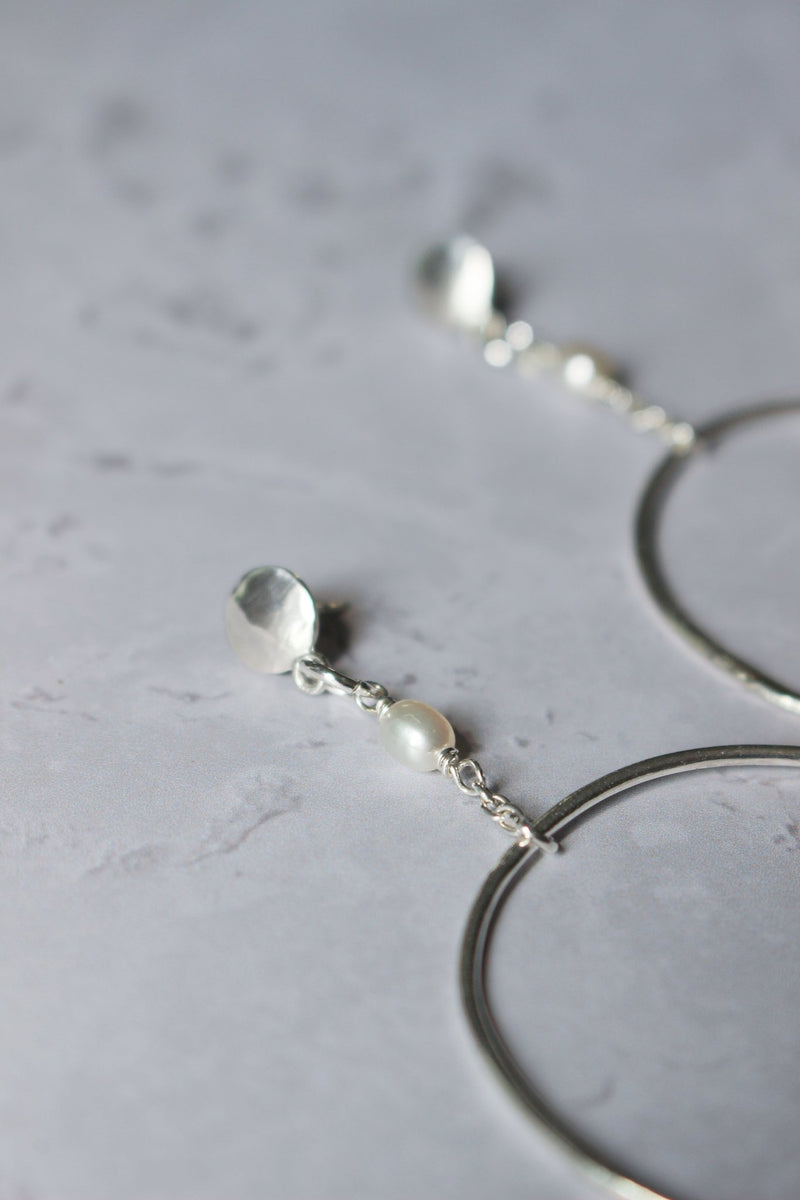 Small silver discs with ear posts drops a short chain with a pearl which connects a handcrafted large silver hoops.