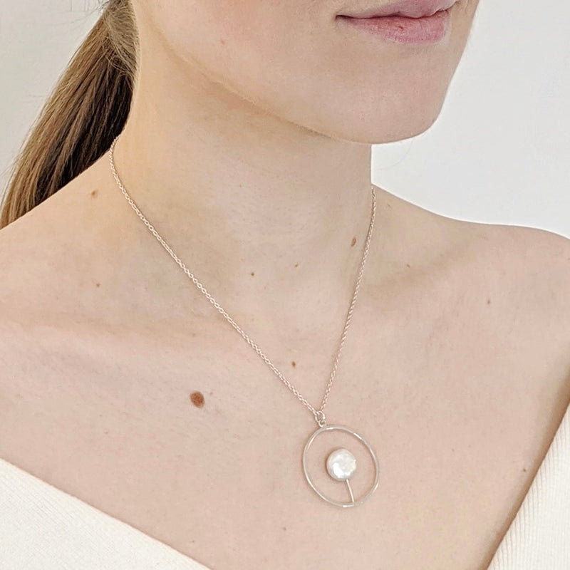 Model wears a handcrafted pendant with an open circle with a white coin pearl attached to the bottom inside of the circle.